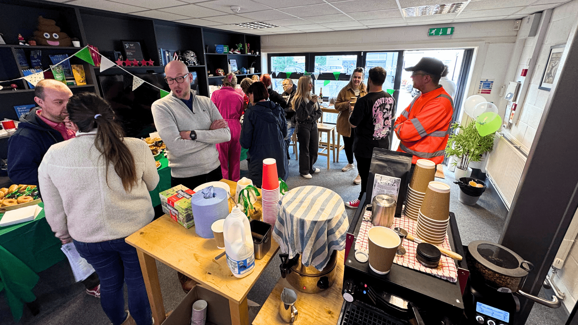 Lots of people in the office front room enjoying cakes as well as chatting together